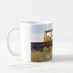 Alter gelber Bulldozer, der auf einer Weide gepark Kaffeetasse
