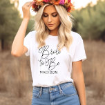 Braut, um schwarz moderne Skript maßgeschneiderte T-Shirt<br><div class="desc">Modernes und lässiges schwarzes Kalligraphieskript "Bride to Be" Frauenbridal Hochzeitstee-Shirt mit individuellem Text, der mit dem Vornamen der Braut personalisiert werden kann. Ideal für die Braut zum Tragen am Junggeselinnen-Abschied und am Hochzeitswochenende!</div>