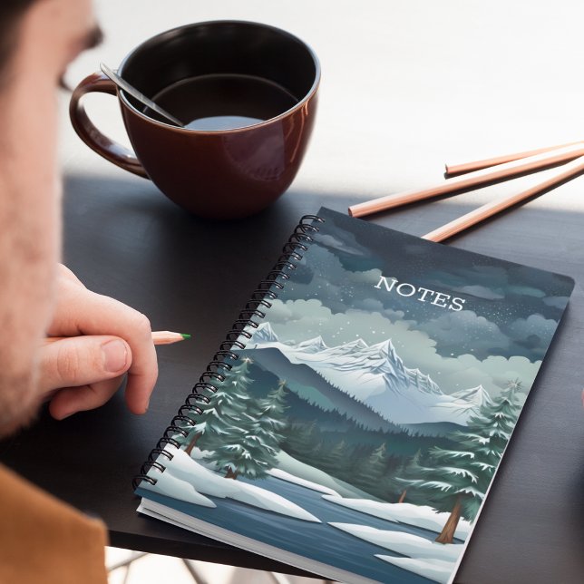 Carnet La forêt d'hiver (A snowy forest mountain scene notebook on a desk with pencils and coffee.)