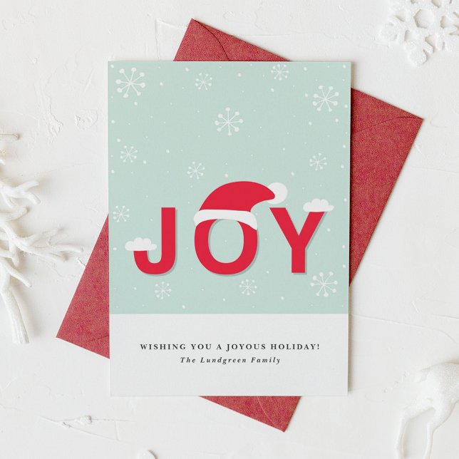 Carte Plat Joyeux À La Neige (This holiday card design showcases the word “JOY” in lettering, playfully topped with a Santa hat.)