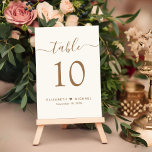 Chic Gold Script Cream Wedding Reception Tischnummer<br><div class="desc">Chic hellcremefarbenes Hochzeitszeichen mit "Tisch" in einem eleganten goldfarbenen Kalligrafieschrift mit Wimpern, die Tischnummer in klassischen goldenen Serifentypografie, Ihre Vornamen verbunden mit einem Herz und Ihr Empfang Datum. Erstellen Sie jede Tischnummer und fügen Sie eine nach der anderen in Ihren Warenkorb, dann Karo aus, sobald alle Zahlen in Ihrem Warenkorb...</div>