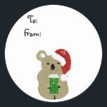 Christmas Koala Bear Runder Aufkleber<br><div class="desc">Ein niedlicher Koala-Bär mit einer roten Weihnachtsmannmütze und einem grünen Geschenk in seinen Pfoten. Passen Sie Ihre Wünsche an.</div>