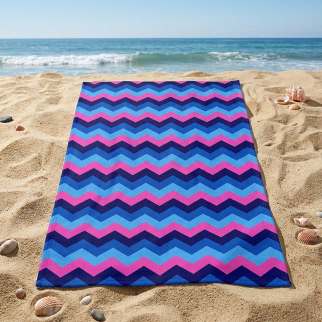 Cooles blaurosa Zickzack Patronenhandtuch Strandtuch (Cool Blue Pink Chevron Pattern Beach Towel laying on sandy beach near an ocean.)
