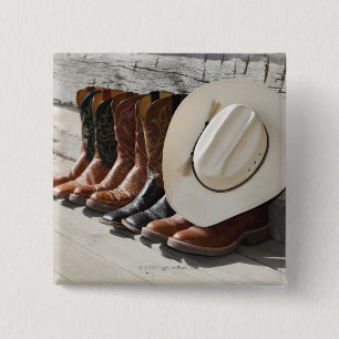 Cowboyhut auf Reihe der Cowboystiefel außerhalb Button