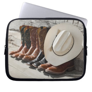 Cowboyhut auf Reihe der Cowboystiefel außerhalb Laptopschutzhülle