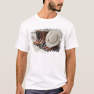 Cowboyhut auf Reihe der Cowboystiefel außerhalb T-Shirt