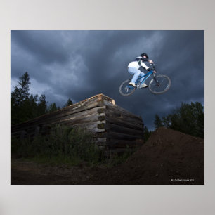 Ein Mountainbiker springt von einer Blockhütte in Poster