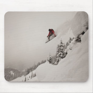 Ein Snowboarder springt von einer Klippe in Puder Mousepad