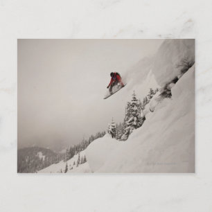 Ein Snowboarder springt von einer Klippe in Puder Postkarte