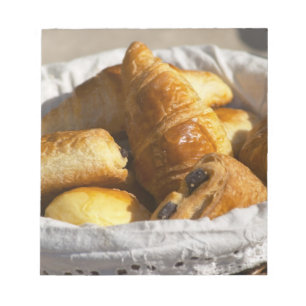 Ein Weiden-Frühstückskorb mit Croissants und Notizblock