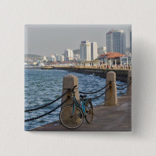 Fahrrad am Wasser mit der Skyline von Yantai Button