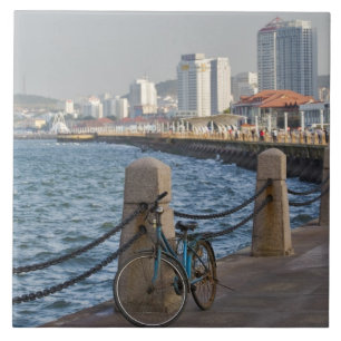 Fahrrad am Wasser mit der Skyline von Yantai Fliese