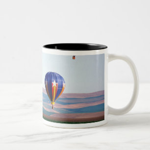 Farbige Heißluftballons schwimmen über Weizen Zweifarbige Tasse