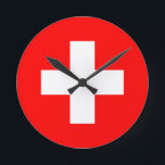 Flagge der Schweiz Runde Wanduhr<br><div class="desc">Die Flagge der Schweiz (Schweizerfahne; Französisch: drapeau de la Suisse; Italienisch: bandiera svizzera; Romansh: bandiera de la Svizra) zeigt ein weißes Kreuz in der Mitte eines quadratischen roten Feldes. Das weiße Kreuz wird als Schweizerkreuz bezeichnet.</div>