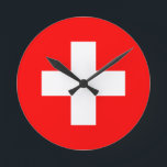 Flagge der Schweiz Runde Wanduhr<br><div class="desc">Die Flagge der Schweiz (Schweizerfahne; Französisch: drapeau de la Suisse; Italienisch: bandiera svizzera; Romansh: bandiera de la Svizra) zeigt ein weißes Kreuz in der Mitte eines quadratischen roten Feldes. Das weiße Kreuz wird als Schweizerkreuz bezeichnet.</div>