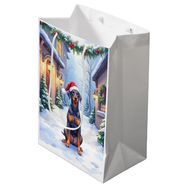 German Pinscher Snowy Courtyard Santa Hat Mittlere Geschenktüte (Vorderseite Schrägansicht)