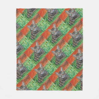 Getigert Katze, die neugierig auf einer Graspelzde Fleecedecke
