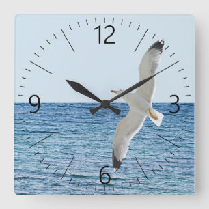 Gull flying above a sea quadratische wanduhr