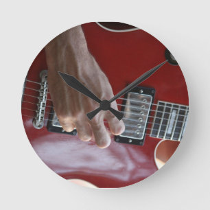 Hand, die rote elektrische Gitarre nahe Runde Wanduhr
