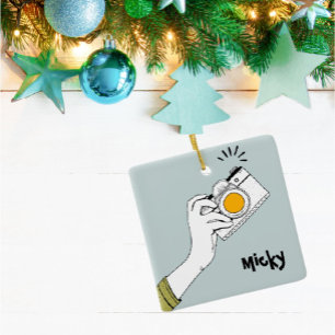 Hand im Cartoon-Stil, die einen Kamera-Schmuck ank Keramikornament