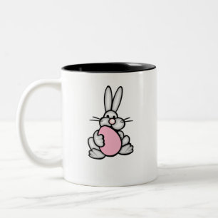 Häschen, das ein hellrosa Ei hält Zweifarbige Tasse