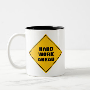 Hellgelbe harte Arbeit vor dem Warnschild Zwei Zweifarbige Tasse