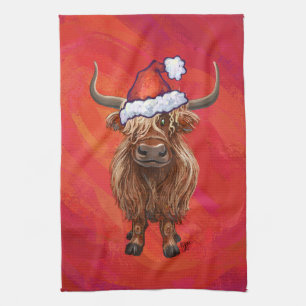 Hochlandkuh in Weihnachtsmannmütze auf Rot Geschirrtuch
