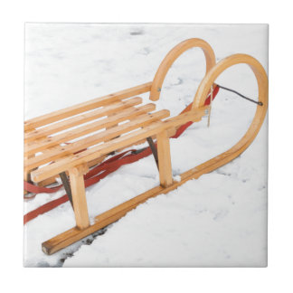Hölzerner Kinderschlitten im Winterschnee Fliese