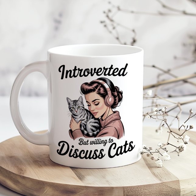 "Introvertiert, aber bereit, über Katzen zu diskut Kaffeetasse ("Introverted But Willing to Discuss Cats" Funny Coffee Mug on a sunny boho kitchen table.)