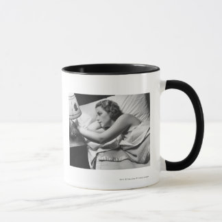 Junge Frau, die auf dem Bett an abstellt Lampe Tasse