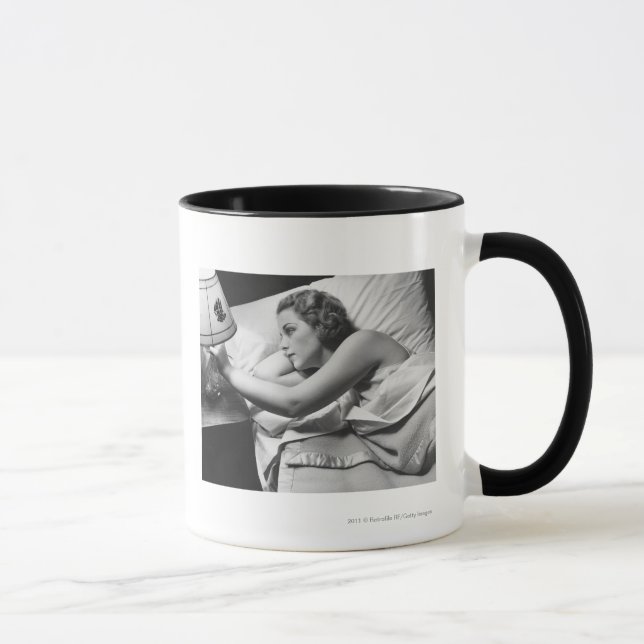 Junge Frau, die auf dem Bett an abstellt Lampe Tasse (Rechts)