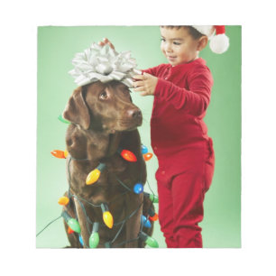 Junger Junge, der Weihnachtslichter um einen Hund Notizblock