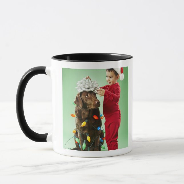 Junger Junge, der Weihnachtslichter um einen Hund Tasse (Links)