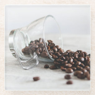 Kaffeebohnen, die sich aus einem klaren Kaffeecup  Glasuntersetzer