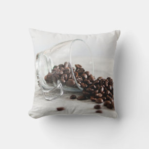 Kaffeebohnen, die sich aus einem klaren Kaffeecup Kissen