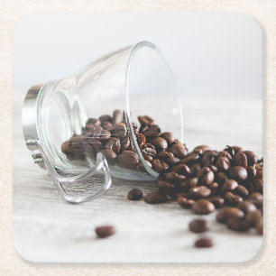 Kaffeebohnen, die sich aus einem klaren Kaffeecup  Rechteckiger Pappuntersetzer
