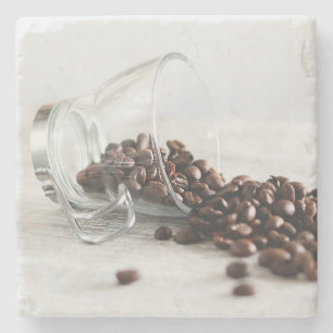 Kaffeebohnen, die sich aus einem klaren Kaffeecup  Steinuntersetzer