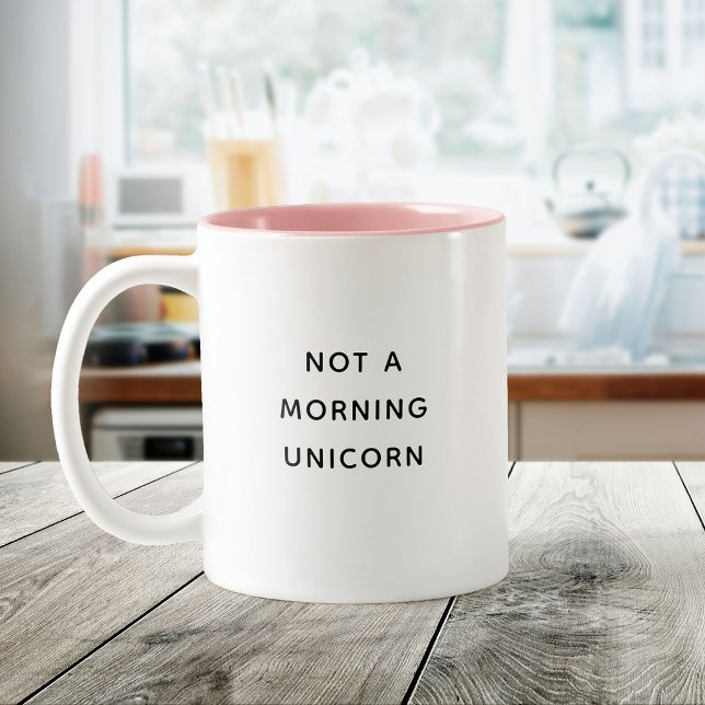 Kein Niedliches Trendangebot am Morgen Zweifarbige Tasse (White mug with pink interior on a wooden table, featuring text "Not a morning unicorn.)