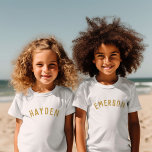 Kinder Personalisiert Name T-Shirt | Gold<br><div class="desc">Diese personalisierten T - Shirt sind mit Kindernamen oder anderen individuellen Texten in einem modernen, stilvollen Schriftart mit gewölbten Bögen versehen, der dem Kleiderschrank eine spielerische und einzigartige Touch verleiht. Diese T-Shirts aus weichem, hochwertigem Stoff sind perfekt für den Alltag, für besondere Anlässe oder als nachdenkliches Geschenk. Lass Deinem kleinen,...</div>