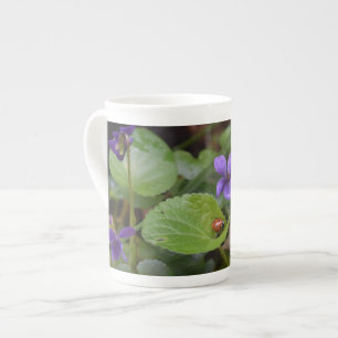 Ladybug über süße Violettsorten-Blume Prozellantasse