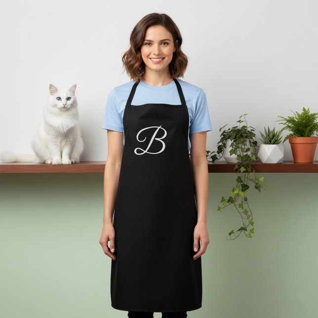 Long tablier noir monogrammé uni (Black apron with large monogram.)