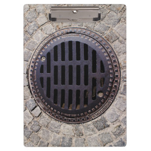 Manhole-Abdeckung und Kopfsteinpflasterstraße Klemmbrett