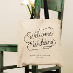Modernes Script Gold Herzlich willkommen in unsere Tragetasche<br><div class="desc">Diese moderne Tasche mit einem minimalistisch lässigen chic Skript-Kalligraphie-Design Lesung WELCOME TO OUR WEDDING sowie Ihre individuelle Namen und Datum der Nuptials bietet saubere Linien zu einem eleganten und raffinierten Aussehen. Der schlichte Stil mit den kleinen, bedruckten Details des Goldenen Herzens verleiht Ihrem Hochzeitstag eine Touch Eleganz. Gute Gastgeschenk Hochzeit...</div>