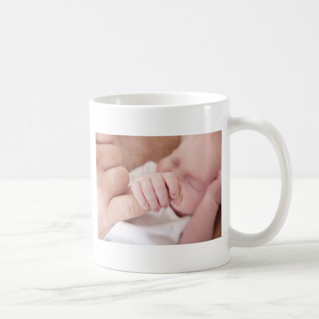 neugeborenes Baby, das Vaterfinger hält Kaffeetasse (Rechts)