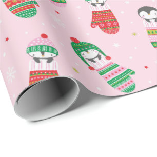 Niedliche Weihnachtspinguine in Fingern in hellros Geschenkpapier