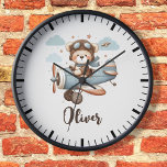 Niedlicher Teddybär Personalisiert Uhr<br><div class="desc">Diese bezaubernde personalisierte Uhr besticht durch einen niedlichen,  skurrilen Teddybär,  der als Pilot mit Hut und Schal verkleidet ist und in einem bezaubernden Zweiflugzeug durch den Himmel ragt. Weich,  pastellfarben und hellbeige Hintergrundfarbe schaffen eine beruhigende und verträumte Atmosphäre,  während flauschige Wolken und funkelnde Sterne eine Touch der Magie ausstrahlen.</div>