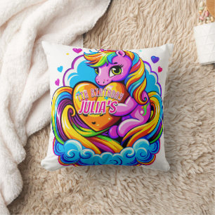 Niedliches Einhorn, das ein Herz-Kissen auf einer  Kissen