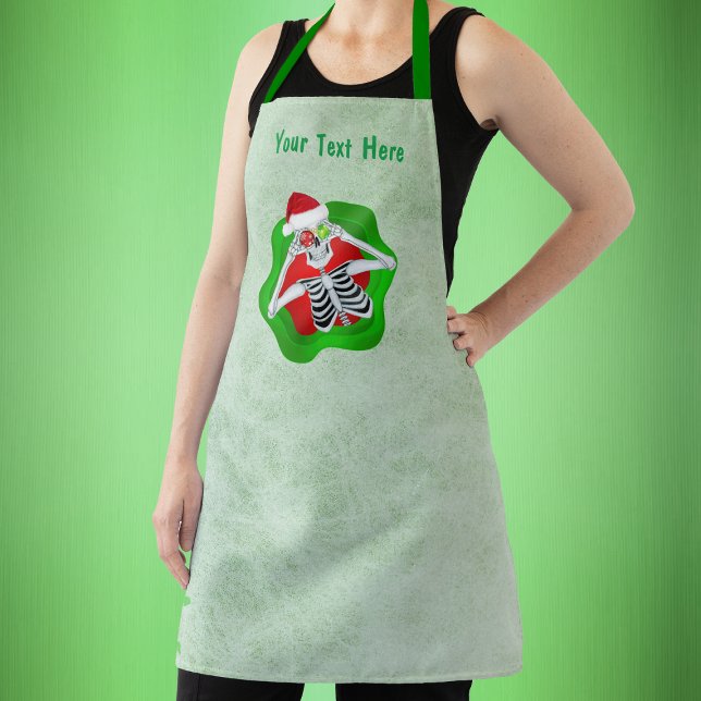 Niedliches Weihnachtsskelett Ornamente Augen im Sp Schürze (Christmas skeleton in splatter shape holding ornaments to eyes on green kitchen apron.)
