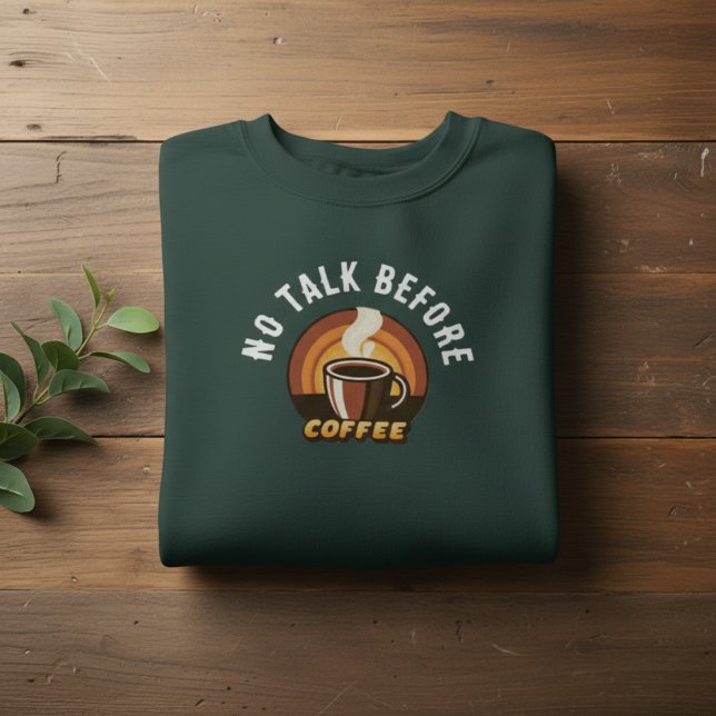 No Talk Before Coffee • Funny Coffee Lover Sweatshirt (folded dark green No Talk Before Coffee sweatshirt on wooden background with leaves)
