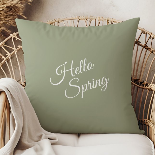 Oreiller de jet Hello Spring vert sauge (Hello Spring Sage Green Throw Pillow in a  boho neutral rattan armchair.)